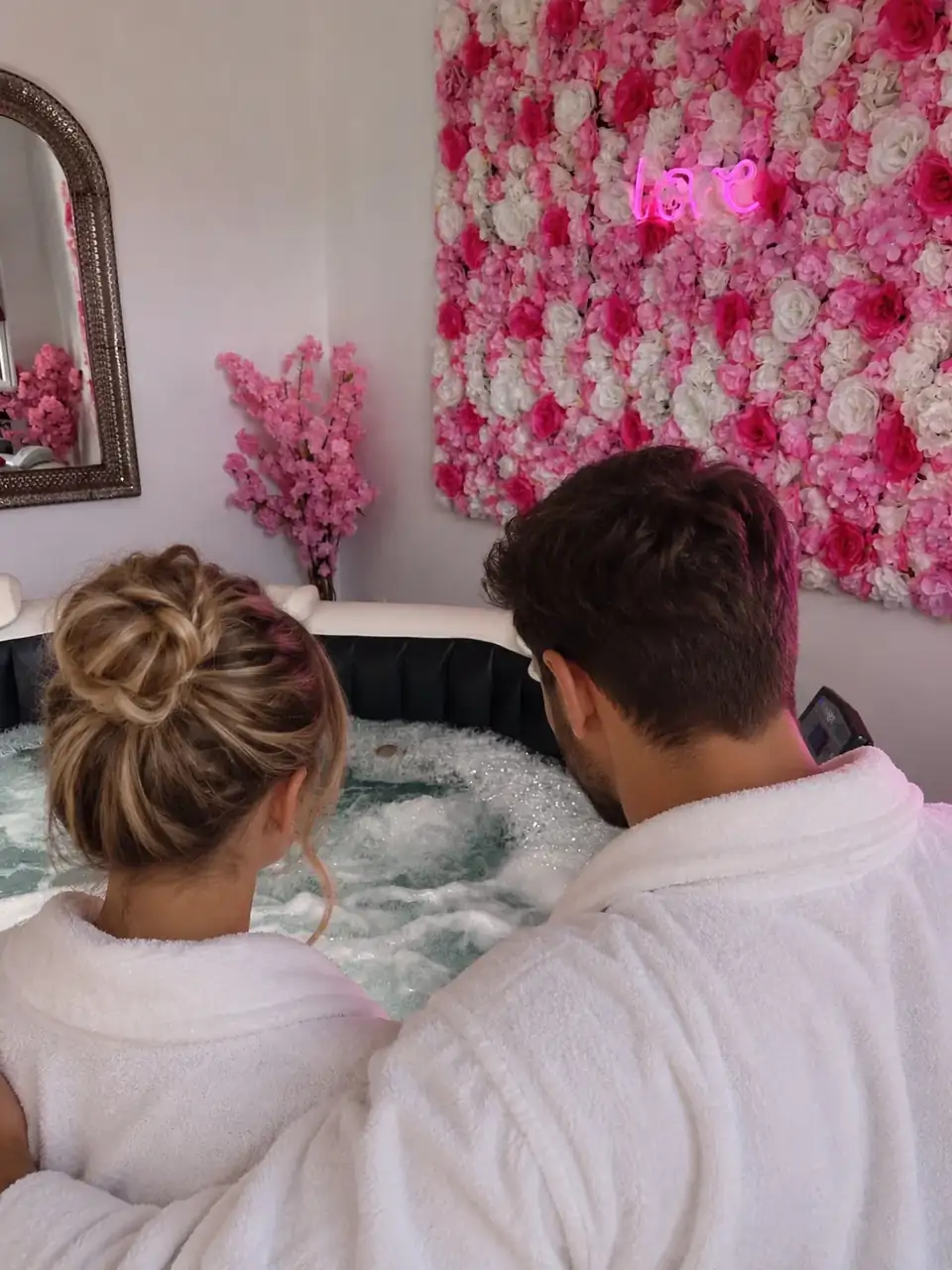 Un couple en peignoir devant le jacuzzi privatif et son mur fleuri